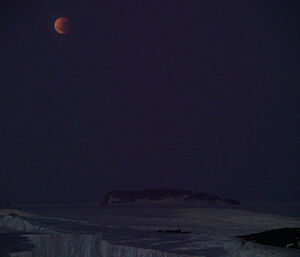 Full moon in partial eclipse over ice plateau which is barely seen in the dark