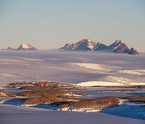 Mawson station seen from a distance with ice plateau behind and snow covered Framnes Mountains in distance