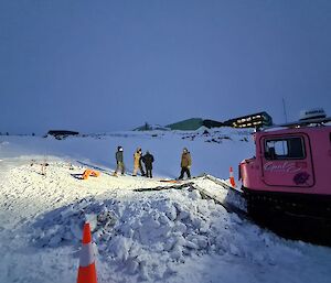 A pink Hägglunds with 4 people in the dark preparing to recover the vehicle on the snow