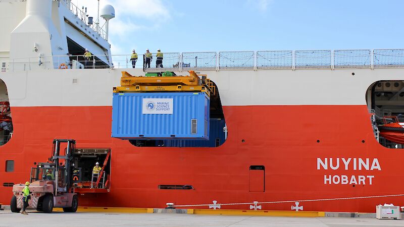 A blue shipping container filled with krill is loaded off a red ship