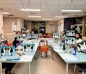 People sitting around the u-shaped table holding up their finished art
