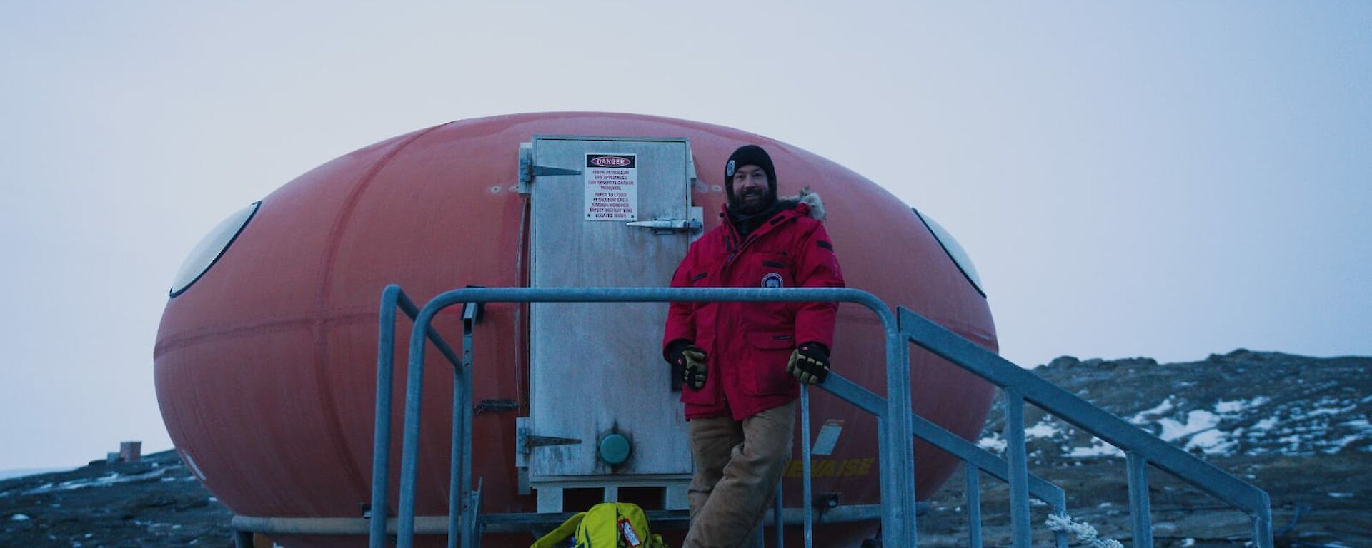 Expeditioner stands on steps leading up door of to melon shaped red hut