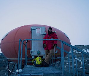 Expeditioner stands on steps leading up door of to melon shaped red hut