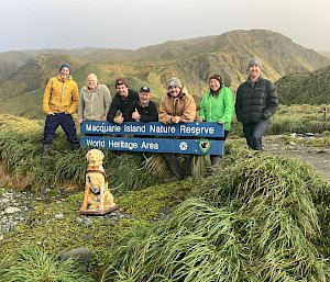 A group of people stand near the Macquarie Island sign with a plastic dog