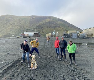 A group of people stand on a grey sandy beach with a plastic dog