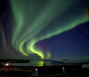 A green aurora lights up the sky over the station's buildings