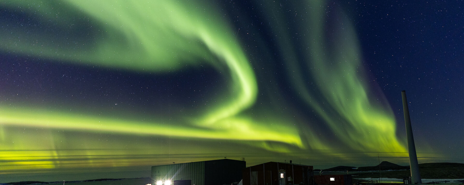A green aurora lights up the sky over the station's buildings