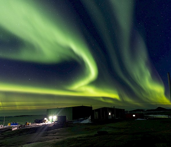 A green aurora lights up the sky over the station's buildings