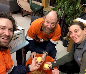 Three people sitting around a bucket peeling potatoes