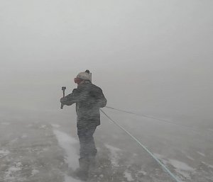 Person with snow whipping around them holding onto blizz line as they walk away from the photographer