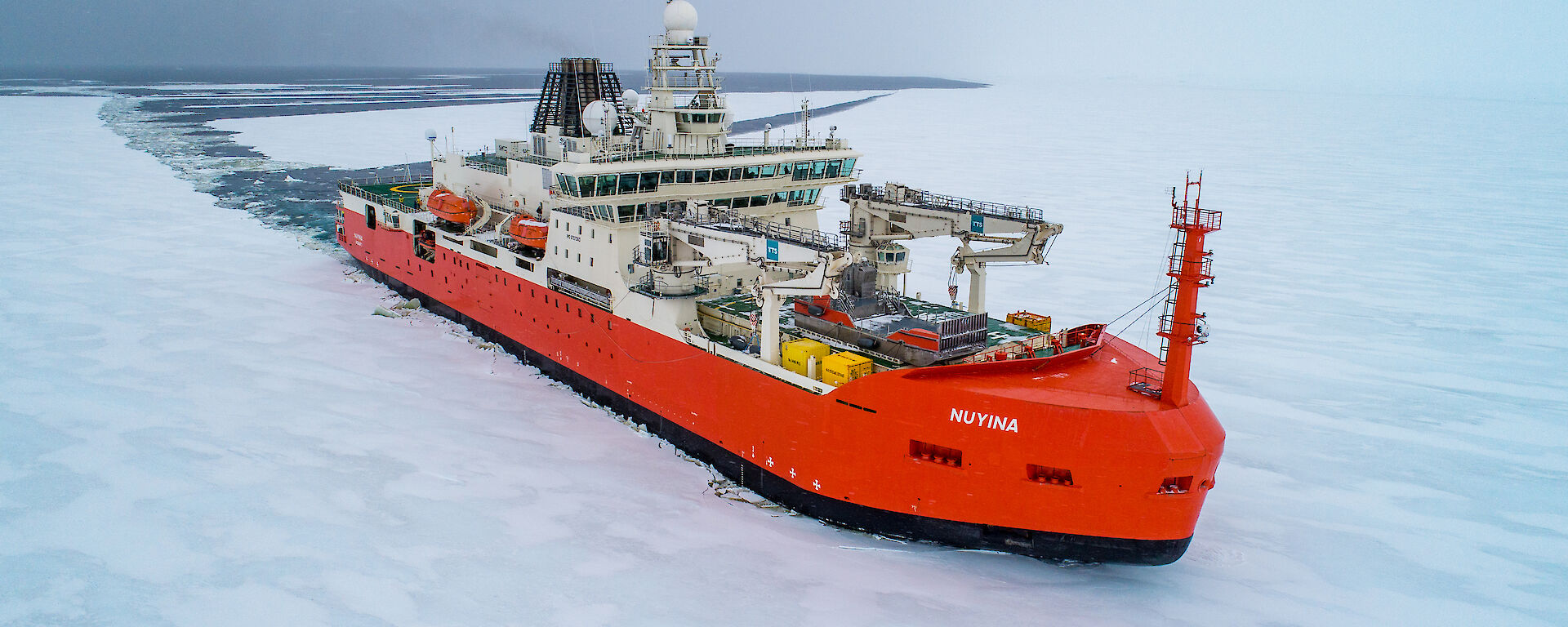 A red icebreaking ship cutting a path through thin sea ice.