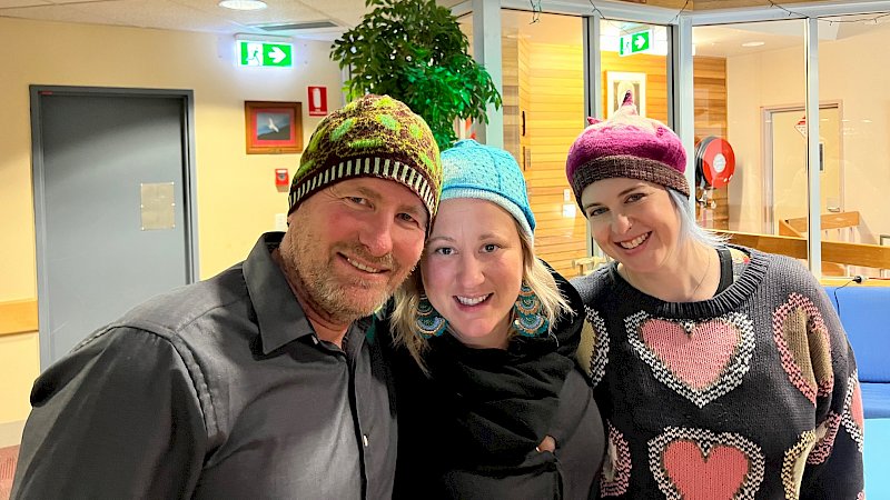 Three people smiling while wearing colourful beanies