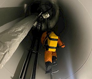 Looking up the inside of the wind turbine at ladder and expeditioner climbing up ahead