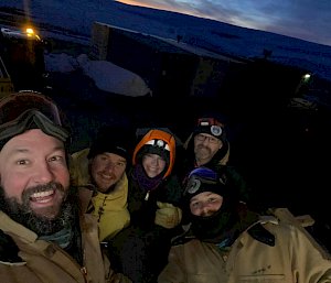 Group of five expeditioners smiling during selfie with sunrise in the background
