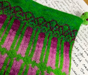 Close up of beanie which is bright green with pink and purple pattern based on the shapes of Diatom and Coccolithopore phytoplankton. Sitting on top of letter from Hadley to the Mawson Expeditioners