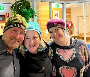 Three people wearing very colourful beanies smiling at the camera