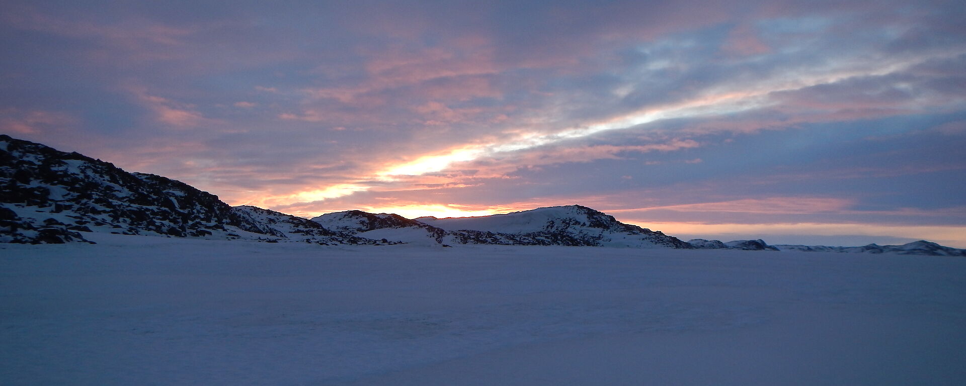 Sky and frozen ocean with mountains with some orange colours showing through the clouds