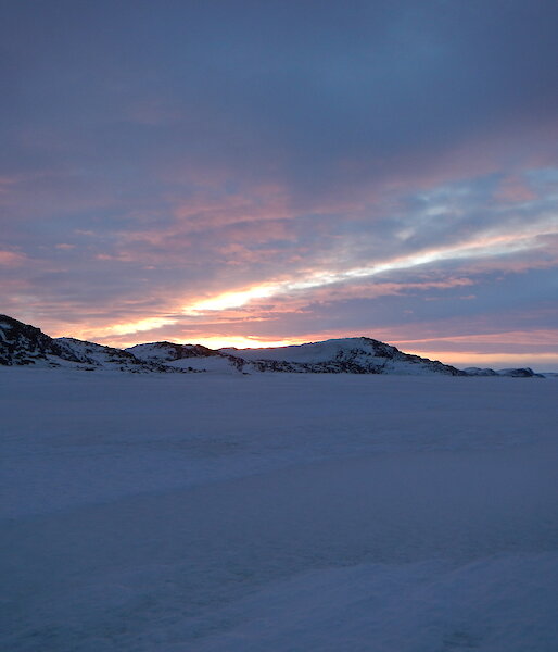 Sky and frozen ocean with mountains with some orange colours showing through the clouds