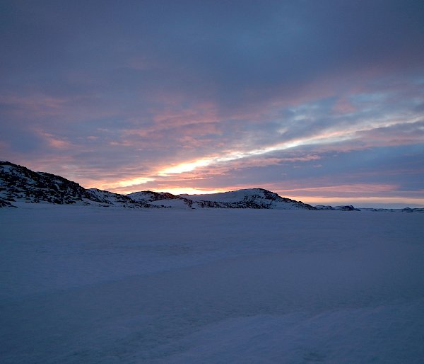 Sky and frozen ocean with mountains with some orange colours showing through the clouds