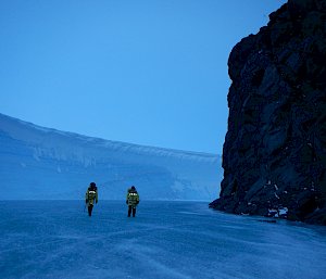 2 expeditioners walking between a ice cliff and rocks