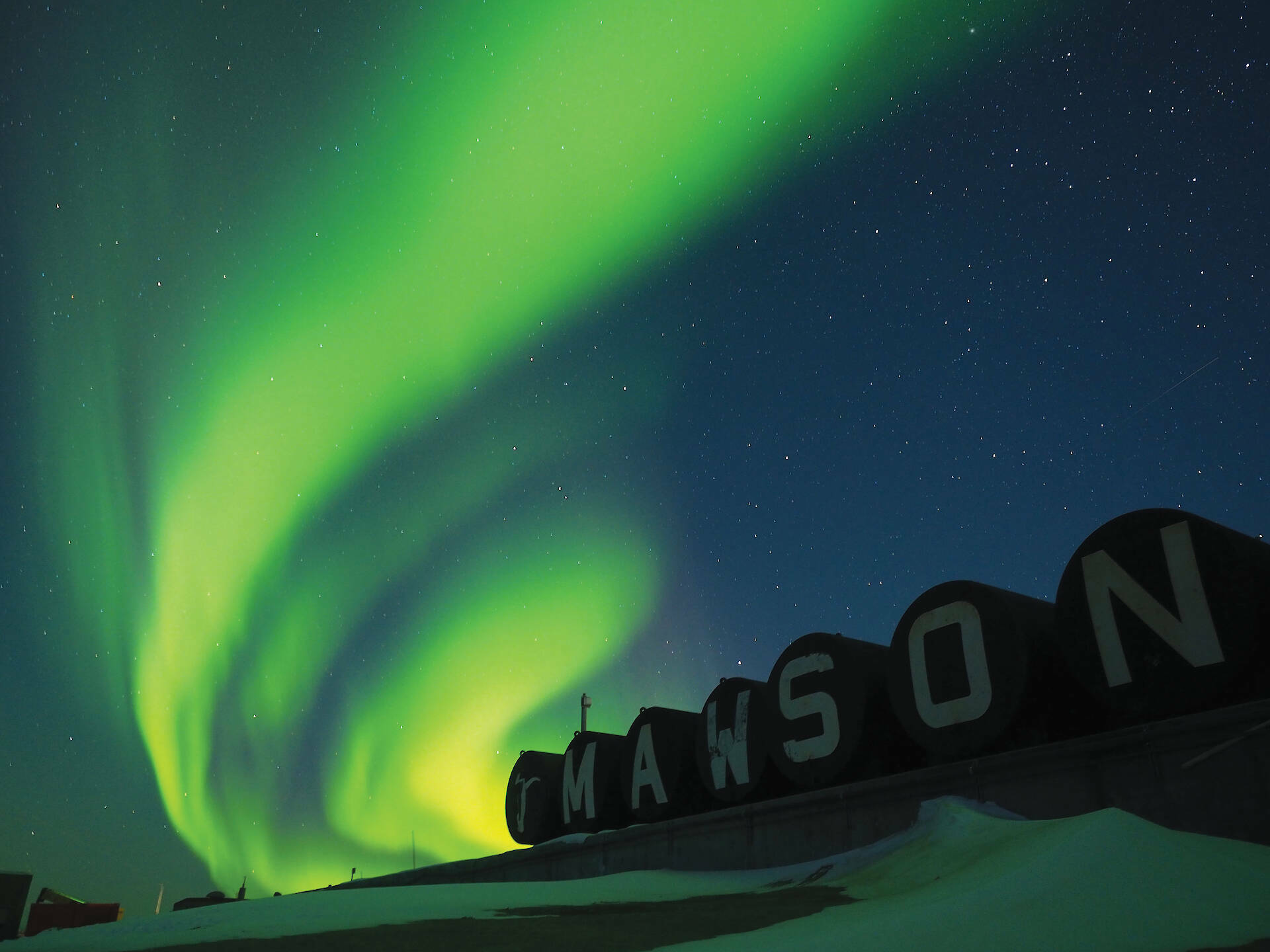 Green aurora over Mawson station sign painted on fuel drums.