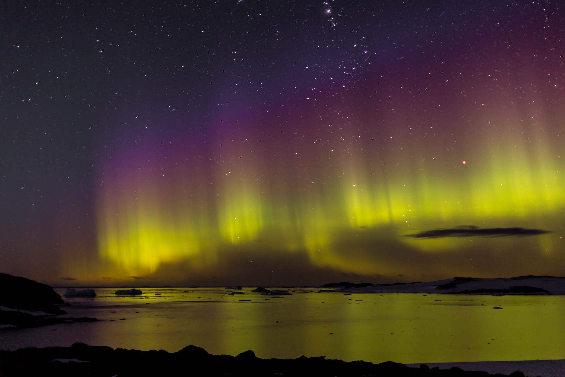 Purple and green aurora over a bay