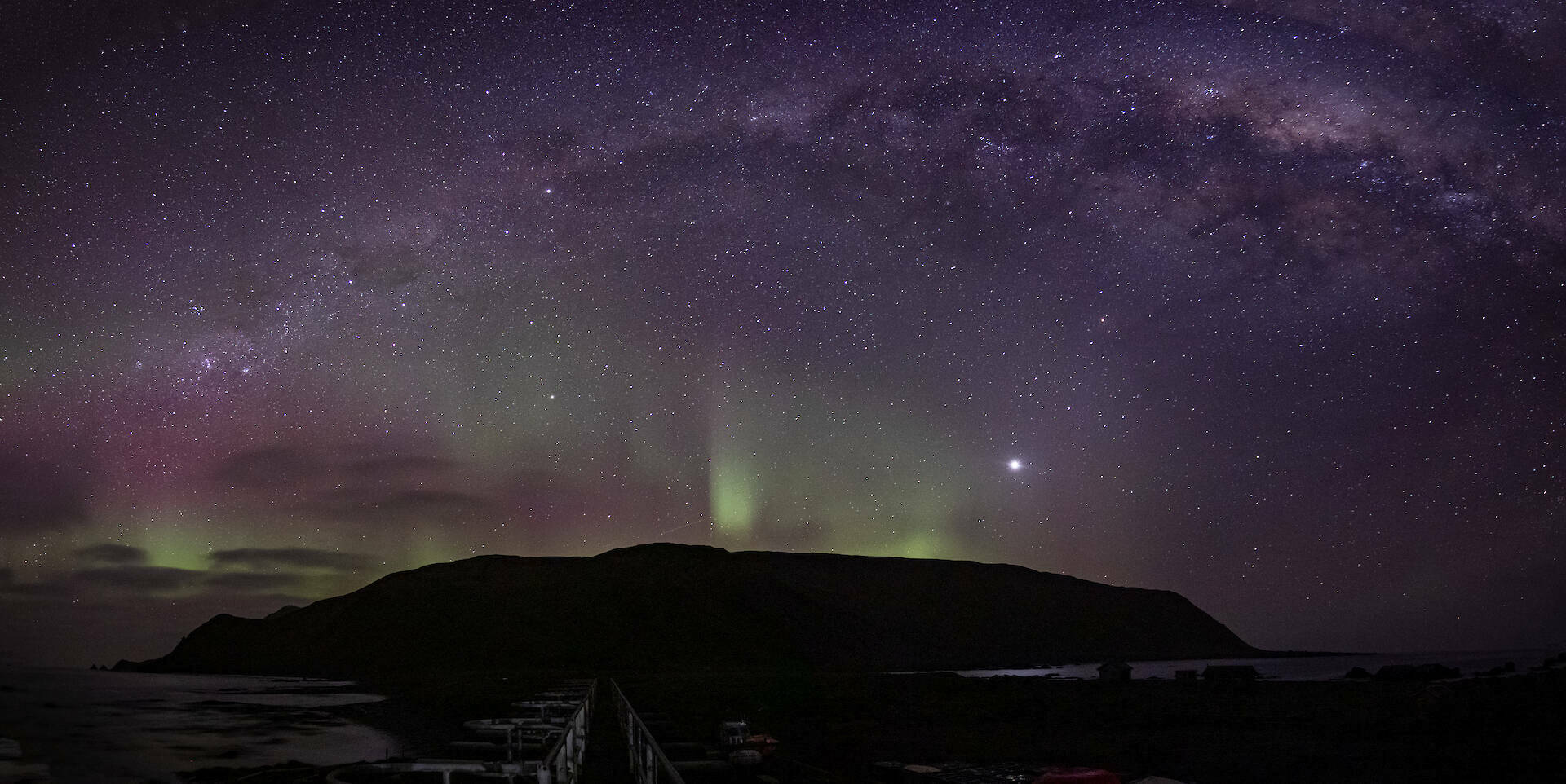 A faint green aurora lights up the sky over Macquarie Island, with the Milky Way visible.