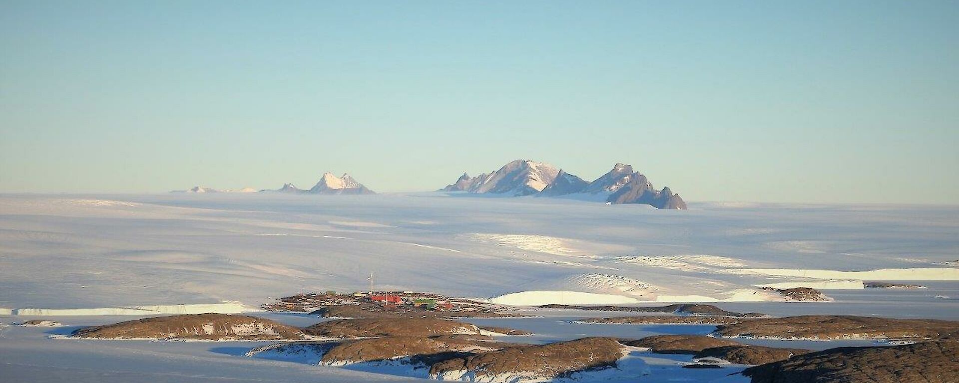 Ice plateau and mountain range in distance, mid distance is the station on the edge of the water