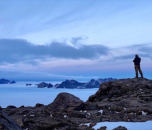 Man stands on mountain ridge with ice plateau and second mountain range behind