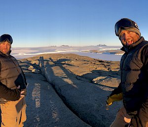 Panoramic shot with same man on left and right of frame, in distance rocky shoreline of antarctica