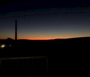 Dark landscape, with orange light peaking out at horizon