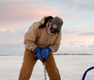 A man using a large drill on the sea ice