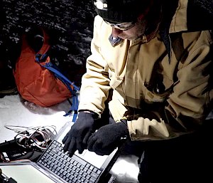 A man typing in to  a laptop on the sea ice in the dark