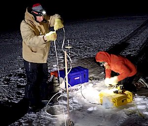 2 men with instruments on the sea ice in the dark