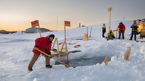 A man sculpts a hole in the ice for swimming