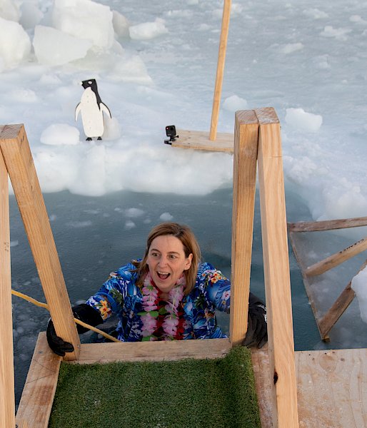 A woman in a Hawaiian shirt climbs out of an ice hole