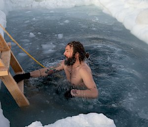 A man emerges from the water in a hole cut through the sea ice