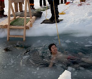 A man floats in water cut through the sea ice
