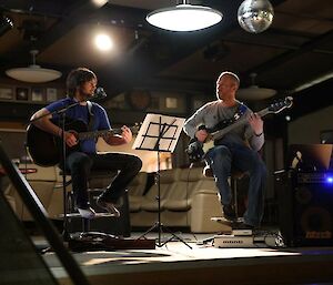 Two guys playing guitars under lights with a shared music stand