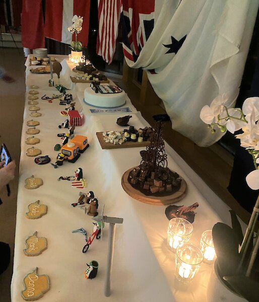 Large dessert buffet table, two-tiered, with penguin montage at front and cake, chocolates and desserts at back