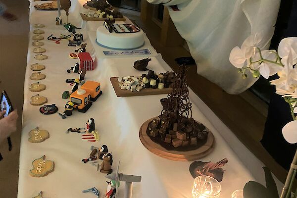 Large dessert buffet table, two-tiered, with penguin montage at front and cake, chocolates and desserts at back