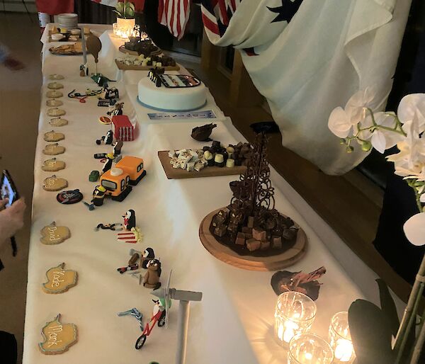 Large dessert buffet table, two-tiered, with penguin montage at front and cake, chocolates and desserts at back