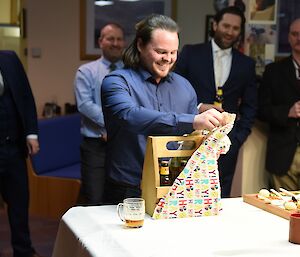 Man with large smile opens gift containing wooden stubby holder, with four men behind watching with great interest