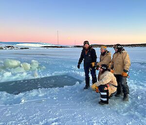 Four men beside rectangular hole cut in sea-ice