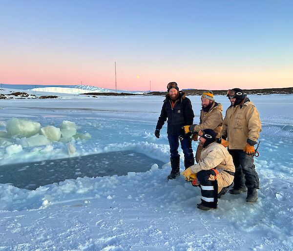 Four men beside rectangular hole cut in sea-ice