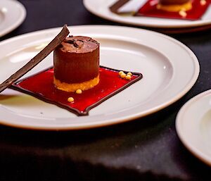 A close-up of a fine dining dessert dish - an arrangement of chocolate mousse, glossy red syrup and thin pieces of chocolate