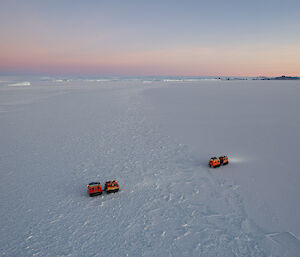 Picture taken from a drone showing two hagglunds one behind the other, travelling across the flat sea ice
