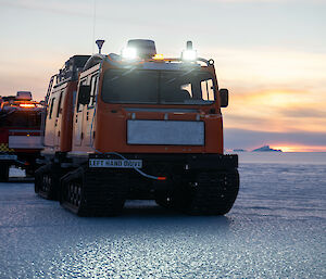 Close up of two hagglunds on flat sea ice with iceberg in distance and twilight colours of pinks and lilacs