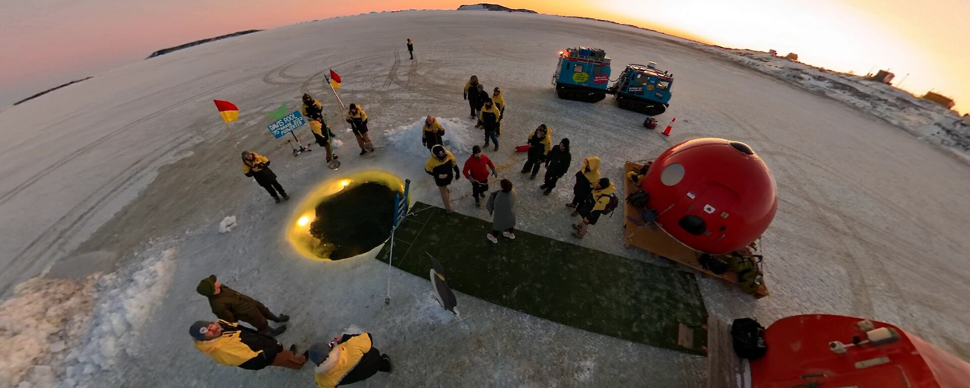 An aerial shot of a round pool in the ice with fake grass and some small huts