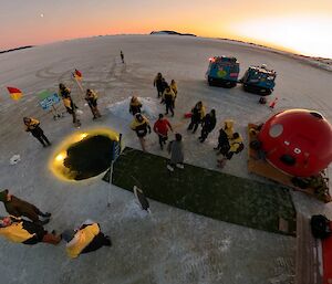 An aerial shot of a round pool in the ice with fake grass and some small huts